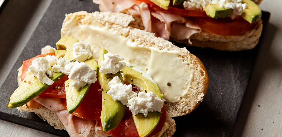 Delicious sandwich roll filled with shavings of ham, tomato, cucumber, feta cheese and a spread of mayonnaise.